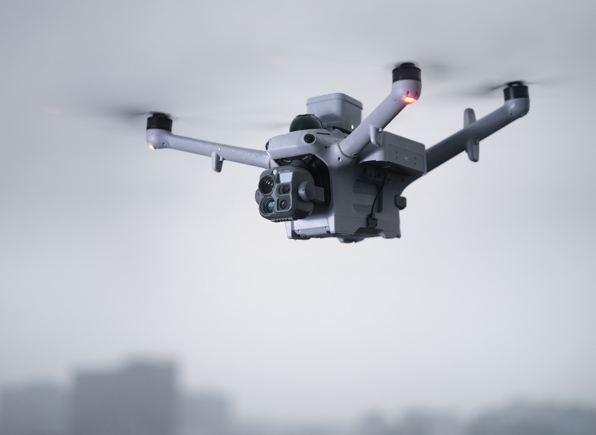 DJI Matrice 5TD mit Lautsprecher und Scheinwerfer im Flug vor städtischer Kulisse